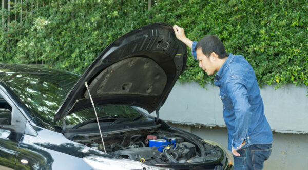 frustrated man looking at car engine on street